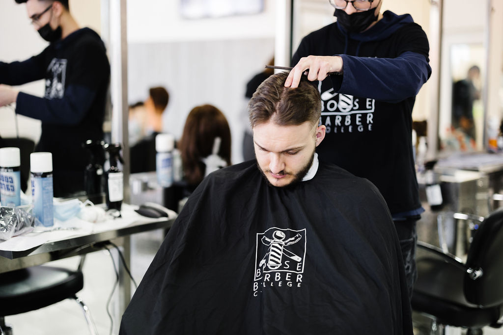 Instructor guiding a student during a haircut on the clinic floor